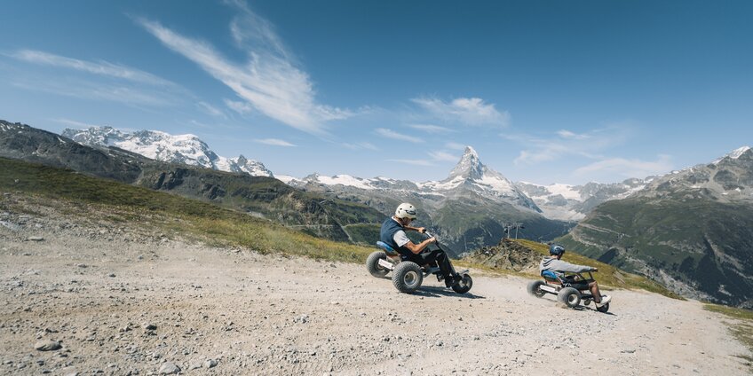 Two men hurtle down the path on mountain carts with the Matterhorn in the background. | © Gabriel Perren